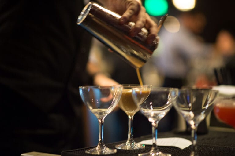 Bartender pouring drinks into martini glasses